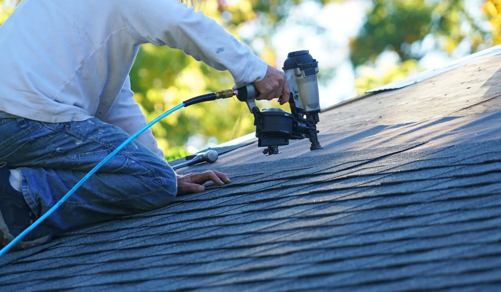 Roofer with nail gun installing shingles during roof replacement.