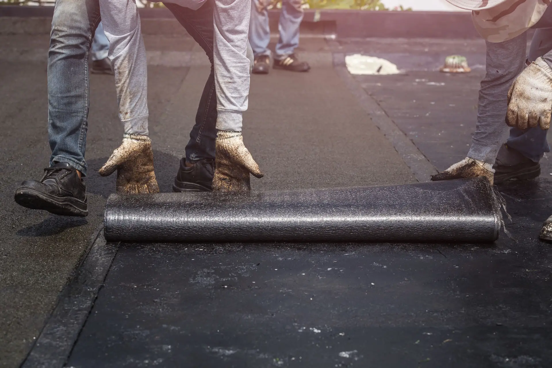 Roofers installing tar foil on the rooftop of building.